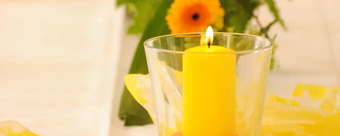 Yellow candle in a large glass in front of a flower arrangement on the "Video" page