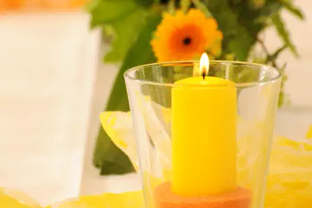 Gelbe Kerze im großen Glas vor einem Blumengesteck auf der Seite Video